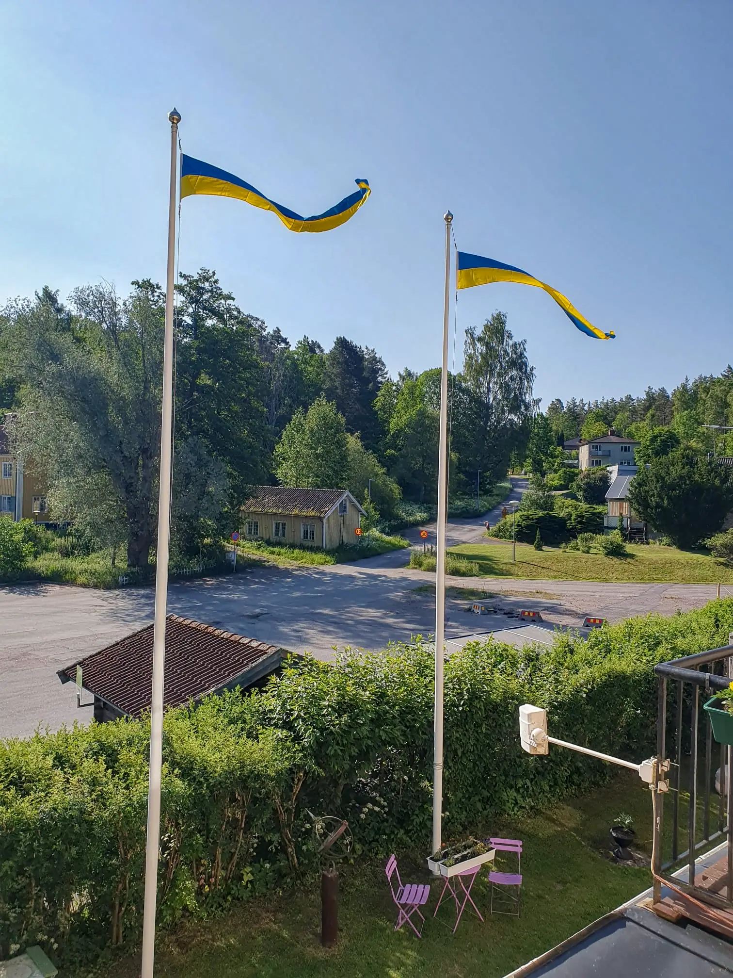 Two Swedish flag pennants flying high over a scenic view of the lush greenery and local houses surrounding Motel E4 in Stavsjö.