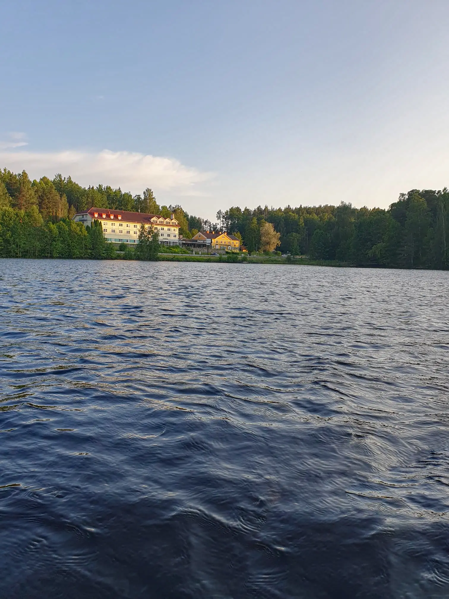 A serene view of a calm lake near Motel E4, featuring gentle ripples on the water and a lush, forested shoreline in the distance.