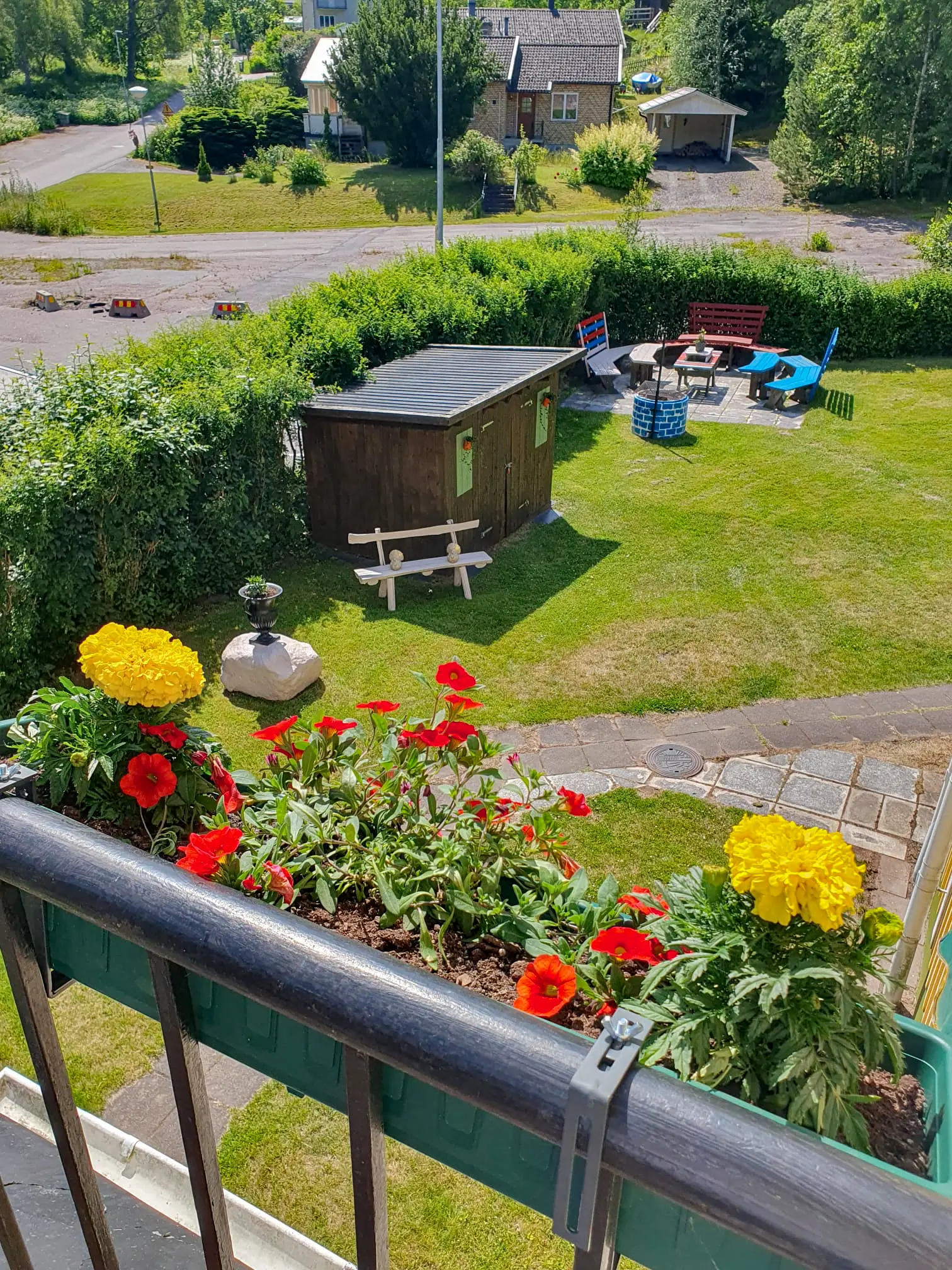View from a balcony at Motel E4 overlooking a lush green lawn with a cozy seating area and vibrant yellow and red flowers in a balcony planter.