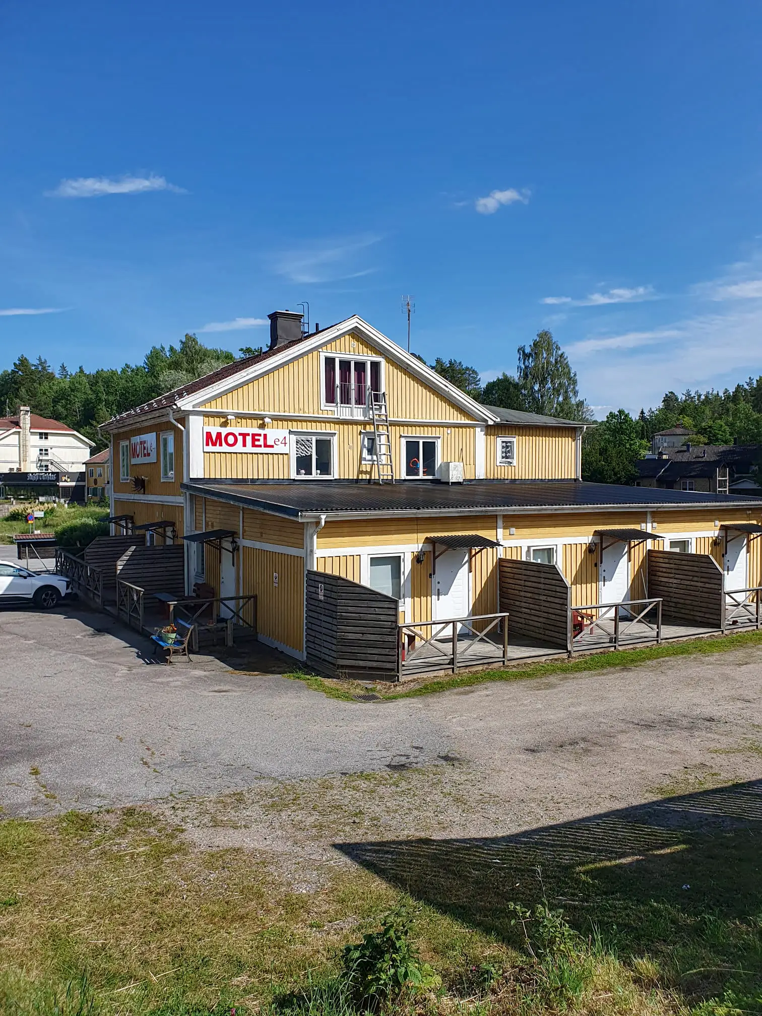 The yellow exterior of Motel E4 in Stavsjö, showing ground-floor guest rooms with private wooden decks and the motel's red and white signage.